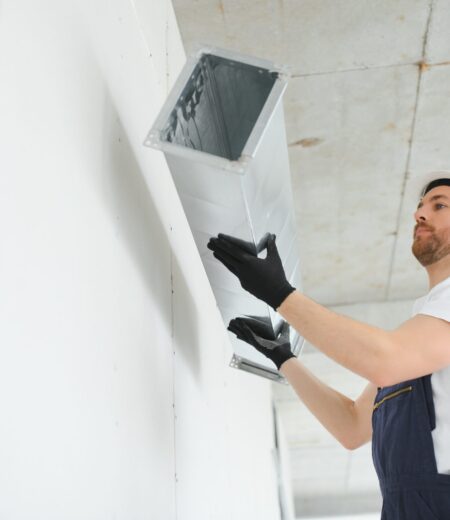 Industrial Theme. Warehouse Heating and Cooling System Installation by Professional Caucasian Technician. Commercial Building Ventilation Rectangle Canals. Air Distribution